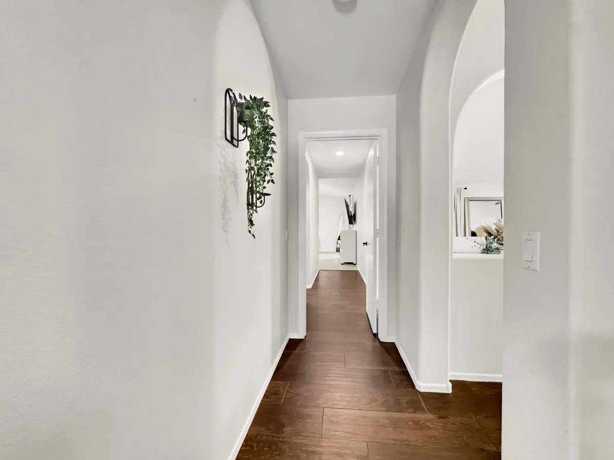 A bright entry hallway with arched doorways, wooden flooring, and a decorative plant, evoking a welcoming transition point between home and the outside world.