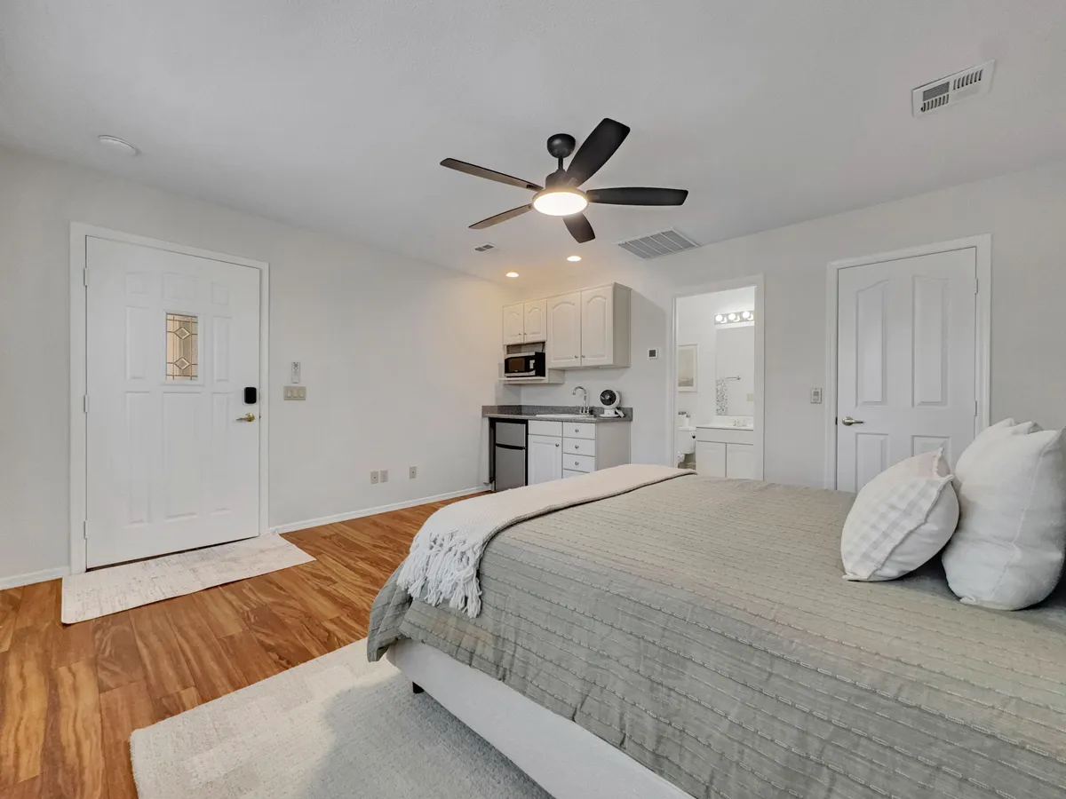 A cozy, separate interior space with a comfortable bed, kitchenette, ceiling fan, and doorway, suggesting the privacy and versatility of a casita. The scene evokes a peaceful spot perfect for reading, remote work, or quiet relaxation.