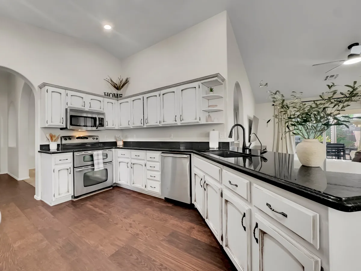 A welcoming kitchen features elegant black granite countertops, crisp white cabinetry, and a decorative plant on the top shelf. The space exudes warmth, with modern appliances and ample room for meal preparation or entertaining. The kitchen is staged for both everyday family use and hosting gatherings, with thoughtful details that invite culinary creativity.