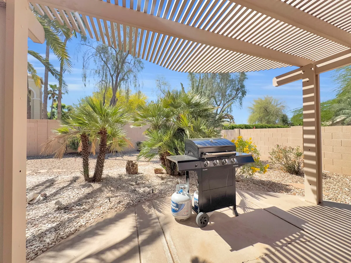 A well-appointed outdoor barbecue area featuring a grill, palm trees, and pebbled landscape. The space is ideal for group gatherings, casual meals, and socializing outdoors in a beautiful and inviting setting.