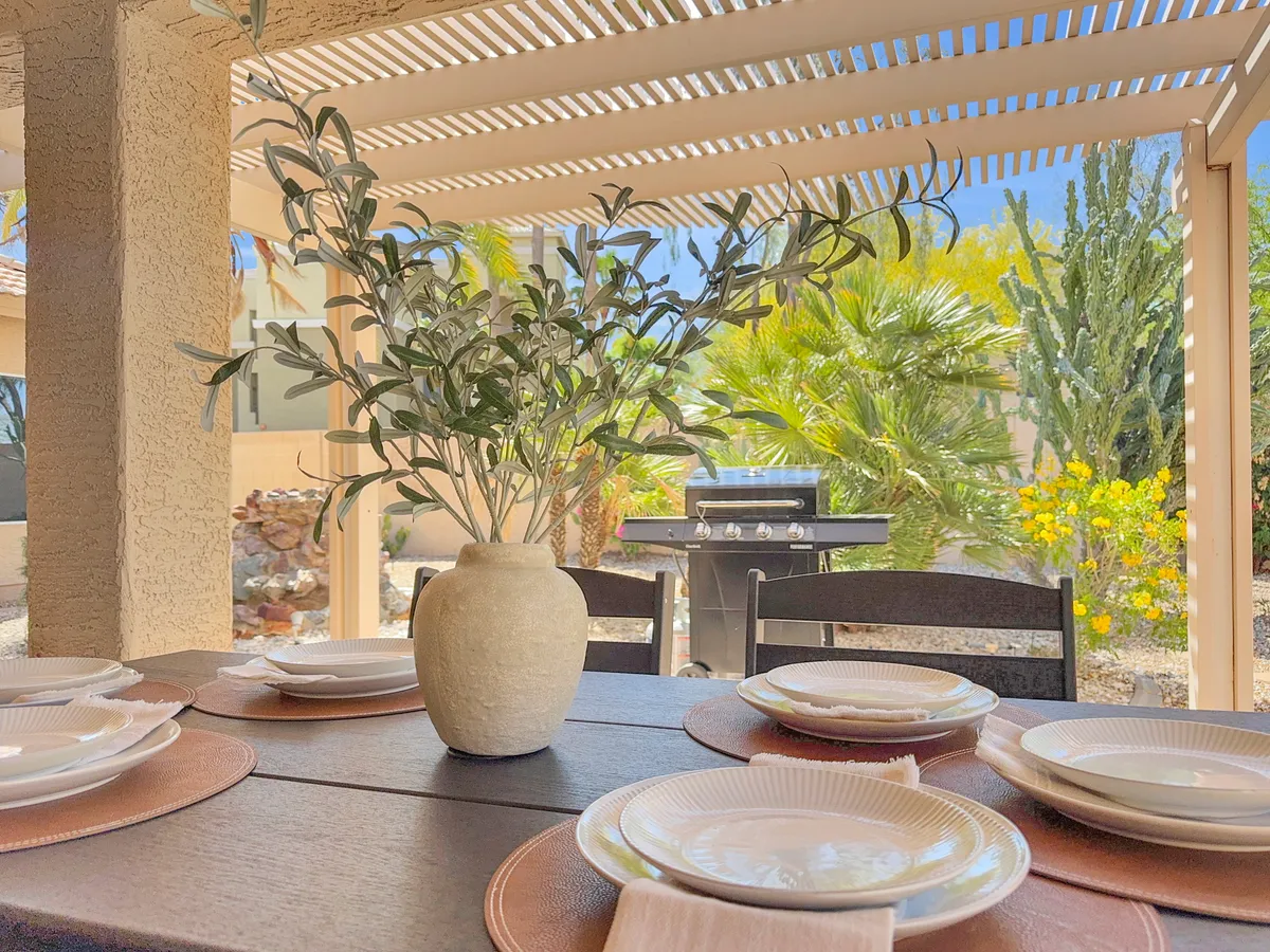 A lush garden setting featuring a dining table set for a meal, a grill in the background, and leafy greenery providing a relaxed backdrop. The scene is ideal for barbecues, weekend brunches, or milestone celebrations with neighbors.