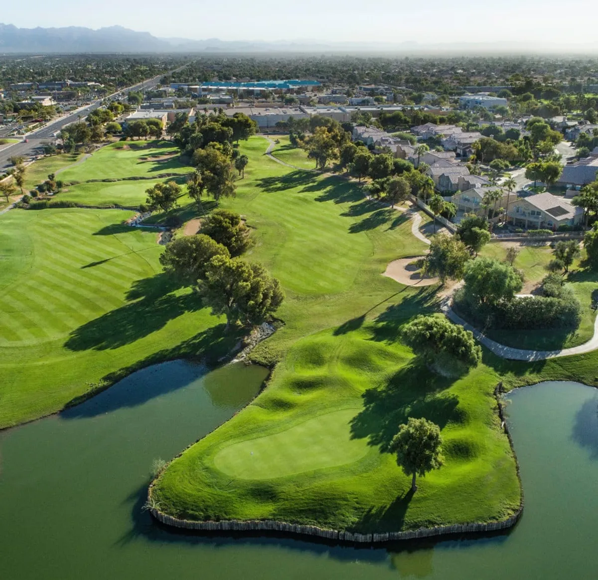 A wide exterior view of a golf course bordered by lush greenery, a serene water body, and nearby residential areas. The scene captures the community amenities just beyond the home, such as open green spaces for recreation and relaxation.