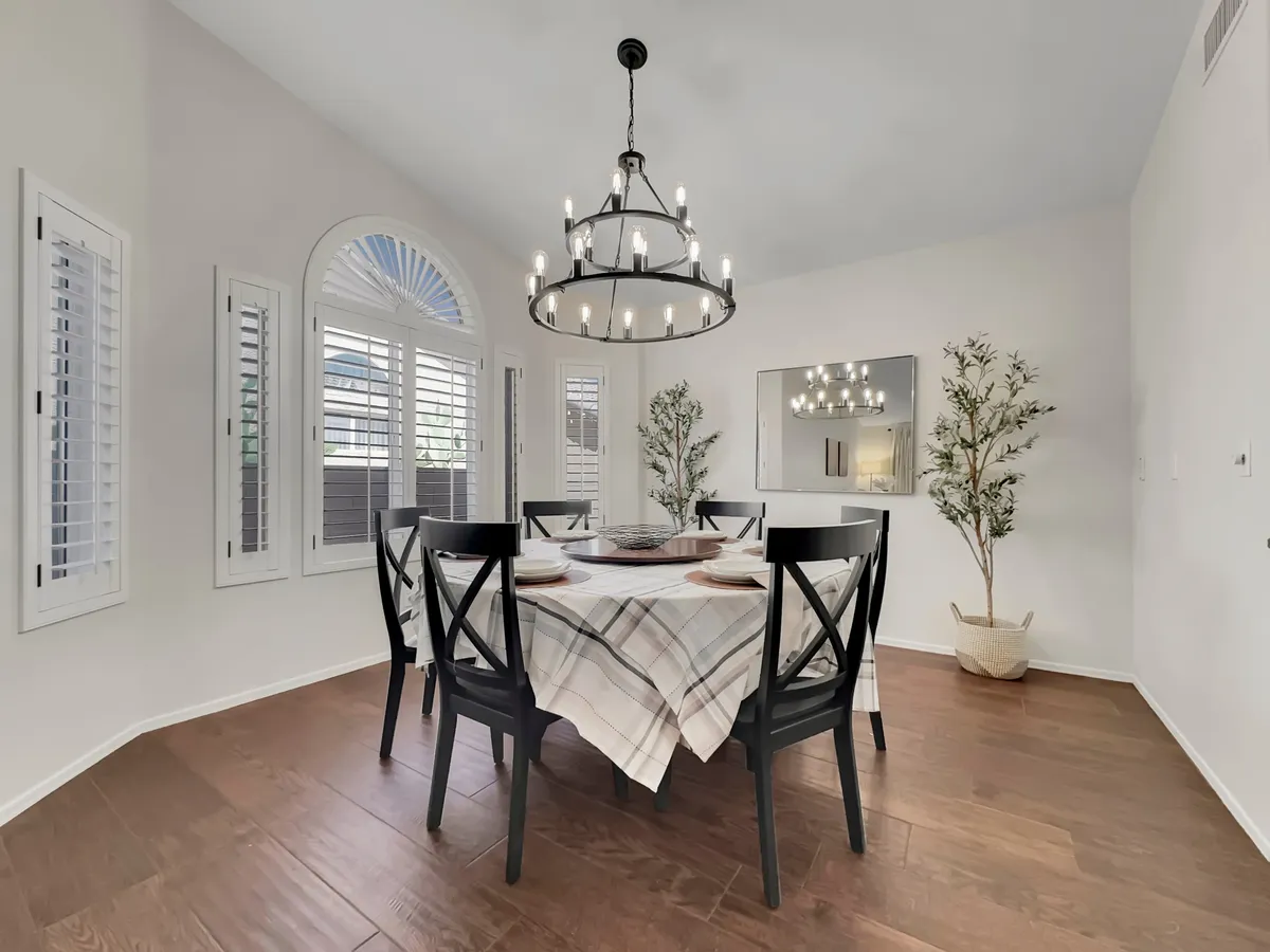 A formal dining table is set beneath a chandelier, flanked by window shutters and decorative plants. The table is arranged for a family dinner or celebratory gathering, with elegant decor and warm, inviting lighting that conveys the importance of shared meals and special occasions.