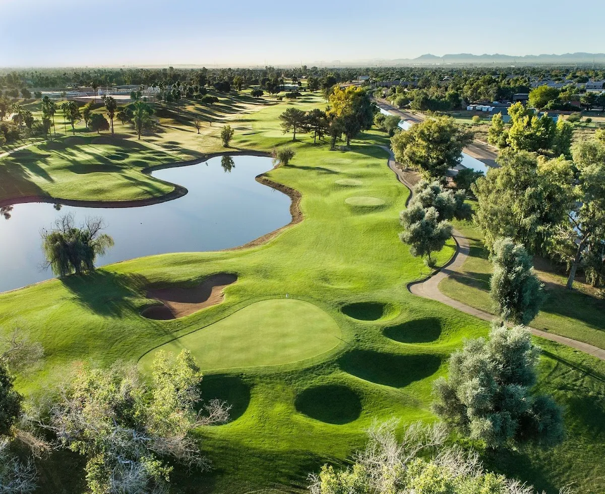 This image features the expansive greens of a golf course, highlighted by a reflective water body and surrounding trees. Golf putting areas are clearly visible, contributing to a serene and active atmosphere.