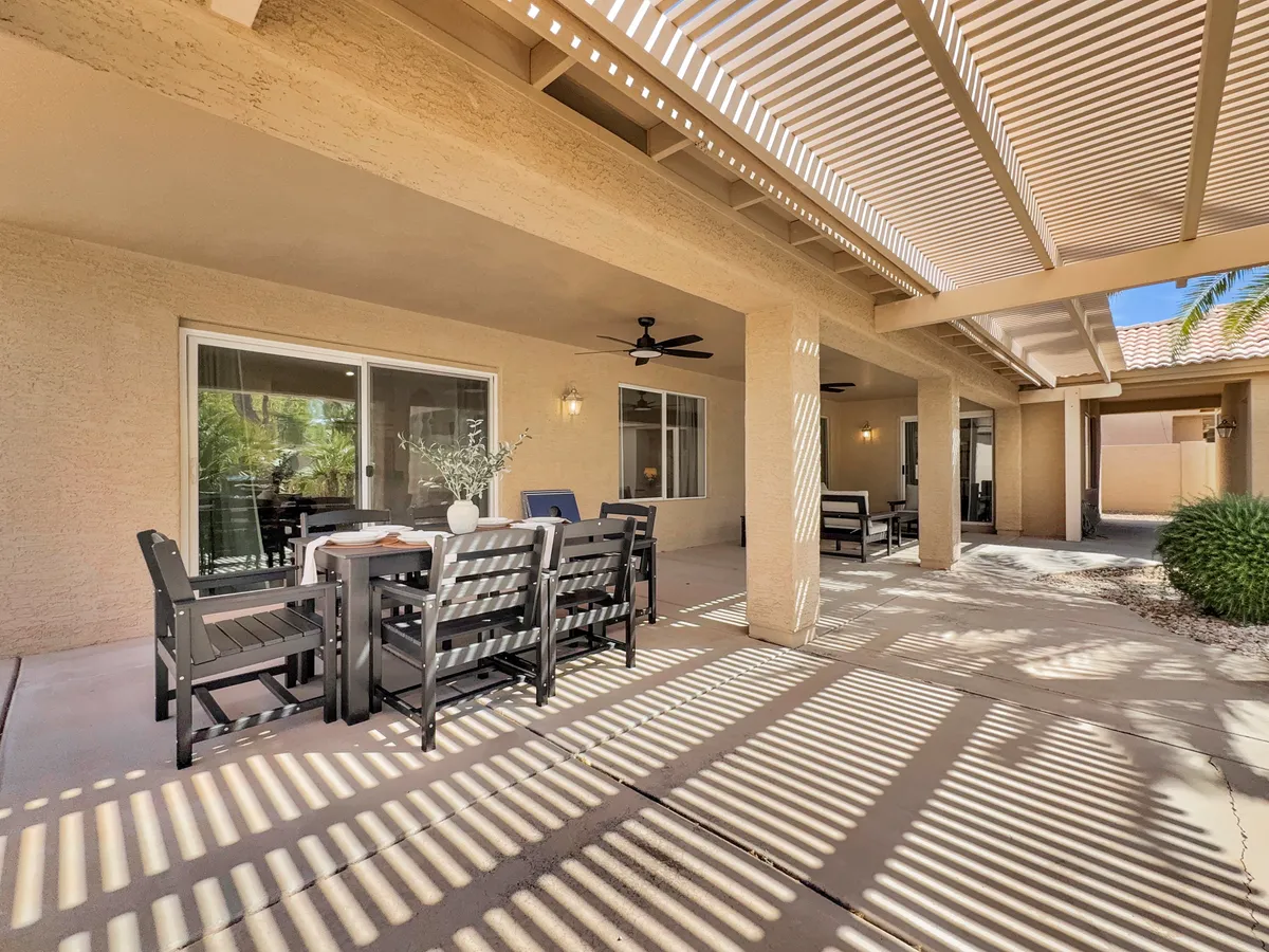 A beautifully landscaped outdoor dining area with a shaded seating space and lush greenery surrounding the table. The setup invites community members to gather for meals or social events in a tranquil, sunlit environment.